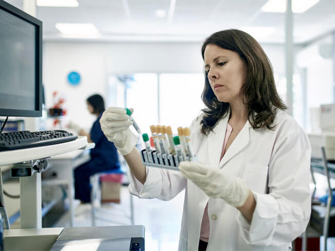Close-up of serious Hispanic female pathologist in white coat examining test tube rack samples in Buenos Aires clinical analysis laboratory.