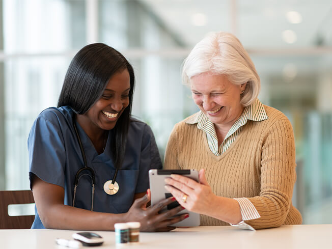 nurse sharing tablet with older female patient smiling