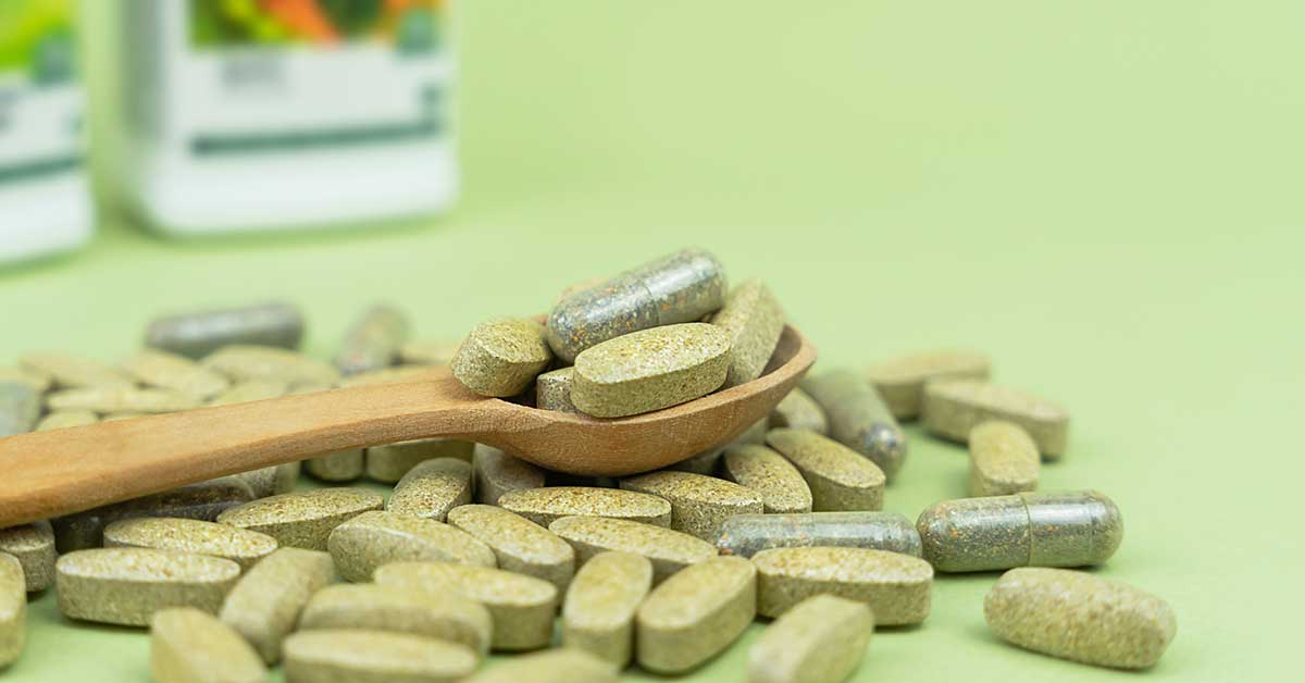 Natural vitamins and supplements in a wooden spoon on a green background