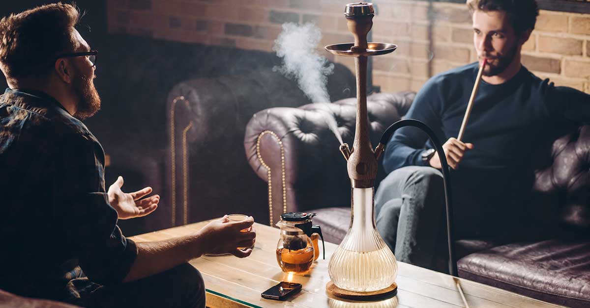 Two businessmen are sitting on the sofas and having a chat and smoking hookah