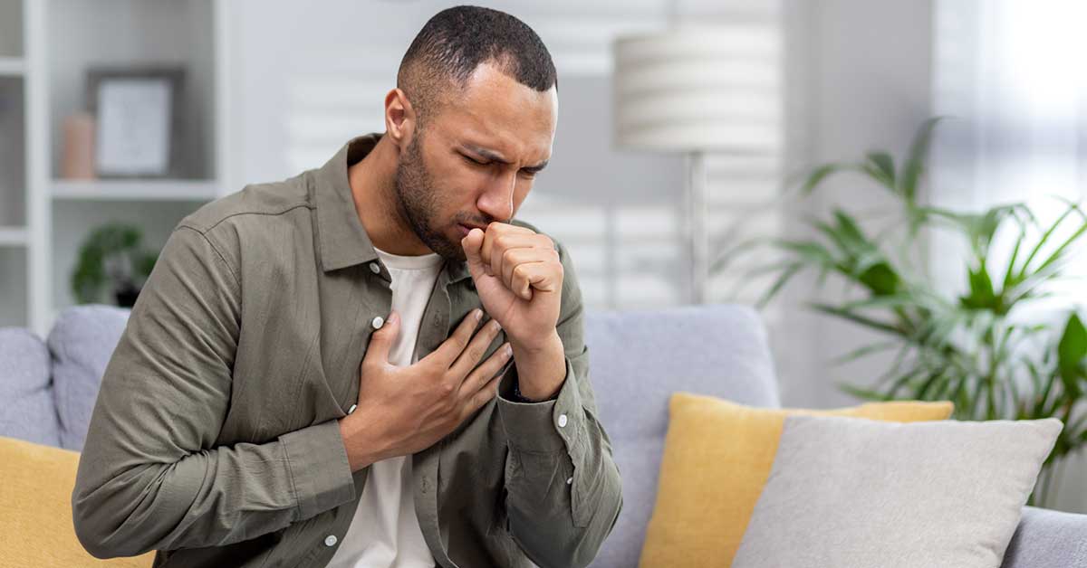 man sitting on the couch at home and coughing