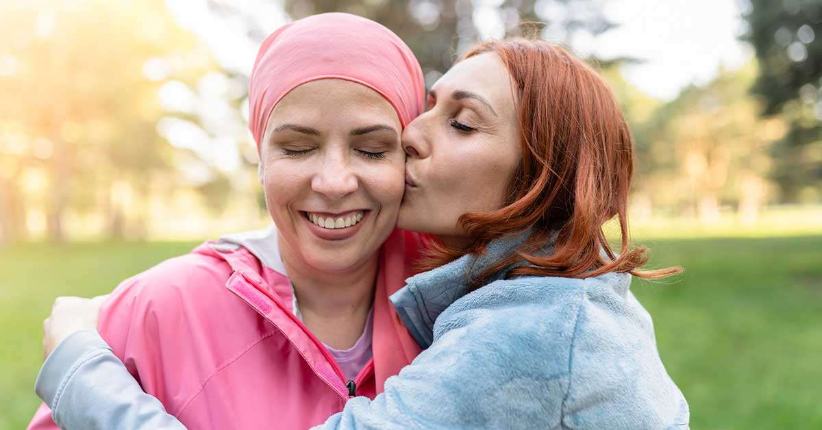 Women hugging with closed eyes while kissing the fighter against cancer