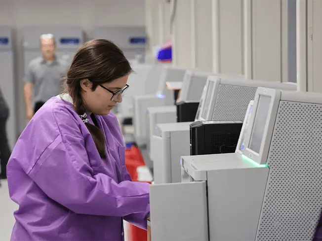 Lab technician operates NGS machine in oncology lab.